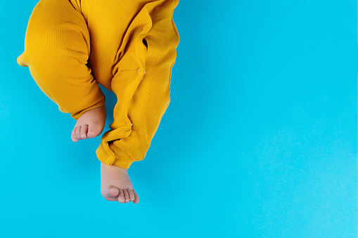 The baby's legs are in yellow pants on a blue background. Mockup for advertising, design, celebration, postcards. Copy space.