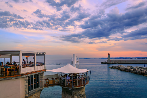 Nice, France - May 28, 2023: Luxury restaurant Le Plongeoir with a stunning view of the Mediterranean Sea and the lighthouse in the harbor at sunset