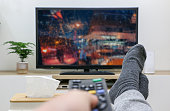 Rainy day concept, feet up at home, holding TV remote control, first-person view streaming and watching television screen.
