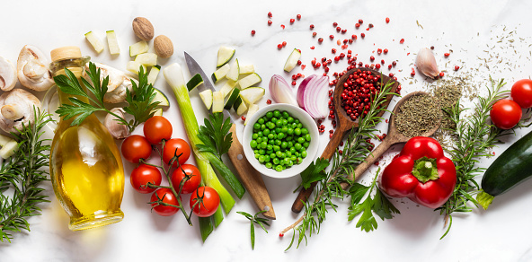 Healthy food cooking ingredients background with fresh vegetables, herbs, spices and olive oil on marble table top view