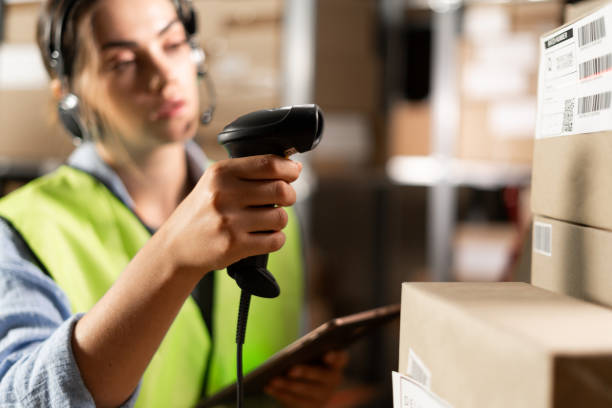 istock woman worker in headset at logistics warehouse using digital tablet. against the background of shelves with cardboard boxes scans a barcode with a scanner. 1669223024