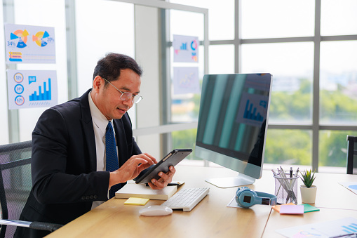 Confident Asian Senior Business Manager at Modern Office Using Digital Tablet for Efficient Corporate Leadership and Growth
