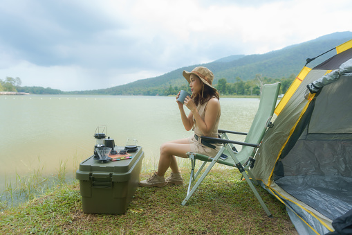 An Asian woman traveler sitting with a camp tent at a natural park, Activity, and lifestyle on holiday, eco-friendly adventures, Happy woman forest or park while camping concept.