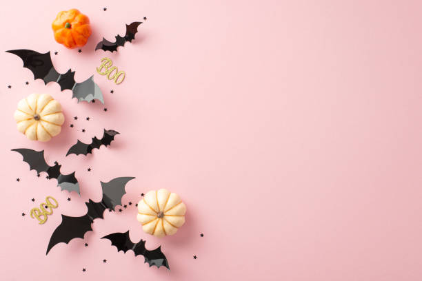 istock Hauntingly delightful display: top view of tiny pumpkins, bones, bats, glittering text boo and black confetti on pastel pink surface, perfect for greetings or ads 1669270560