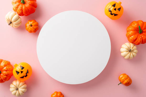 Modernized Halloween themed layout. Top view capturing thematic elements: small carved pumpkins on pastel pink background. Empty circle for greetings or advertisements