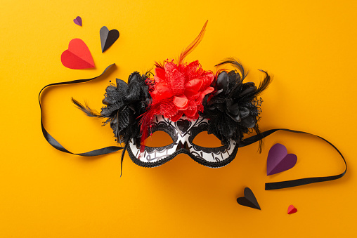 Vibrant top view of carnival mask, a flowery skeleton with lace, paper hearts. Orange background, perfect for advertisements