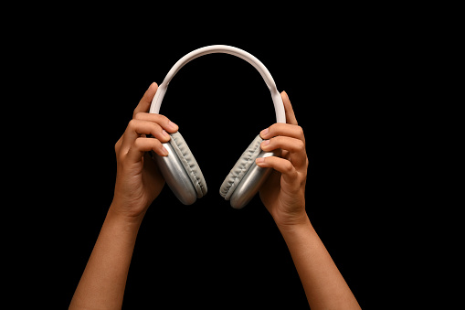 Hand holding wireless headphones isolated on black background. People, entertainment, technology concept.