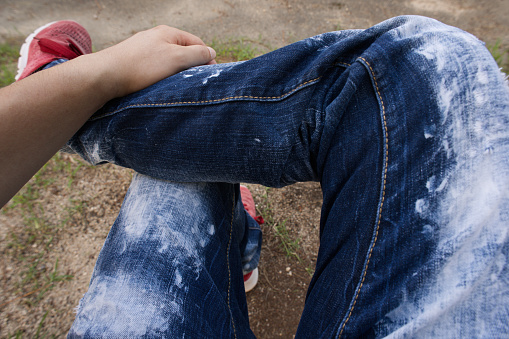 Person in jeans and shoes posing up against a wall. 