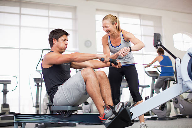 Personal trainer with man on rowing machine in gymnasium  fitness trainer stock pictures, royalty-free photos & images