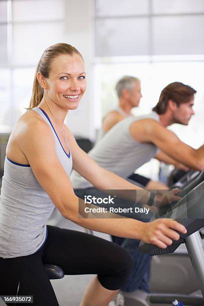 Retrato De Mujer Sonriente En Máquinas De Ejercicios En El Gimnasio Foto de stock y más banco de imágenes de Bicicleta estática