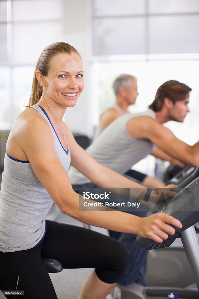 Retrato de mulher sorridente no aparelho de musculação na sala de ginástica - Foto de stock de Bicicleta Ergométrica royalty-free