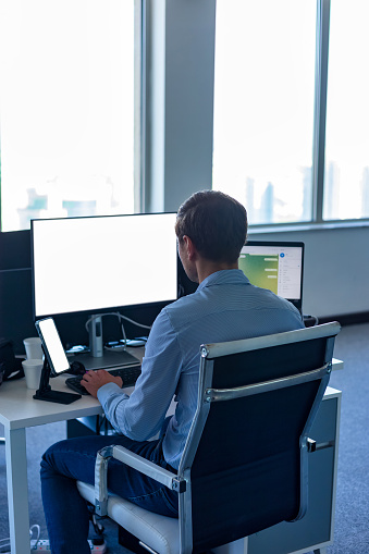 Rear view of man businessman manager works in corporate office. Male broker agent in blue shirt using computer at desk, from behind. Business development growth, solutions concept. Copy ad text space