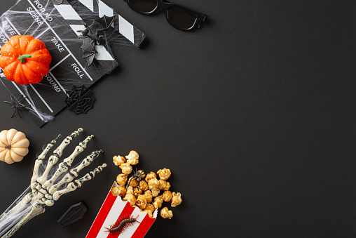 Elevate your Halloween entertainment with top view photo featuring cinema popcorn, clapper and eerie Halloween-themed decorations on a black isolated background, ready for your promotional efforts