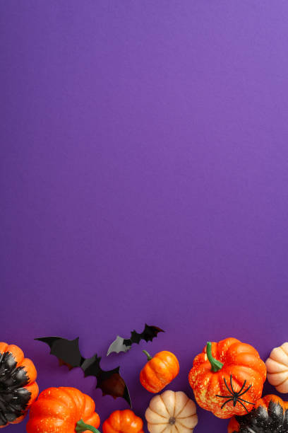 istock Dive into Halloween fun with this creative arrangement. Vertical top view shot of thematic decor, petite pumpkins, spectral spider, bats on violet backdrop with a blank space for greetings or ads 1669373748