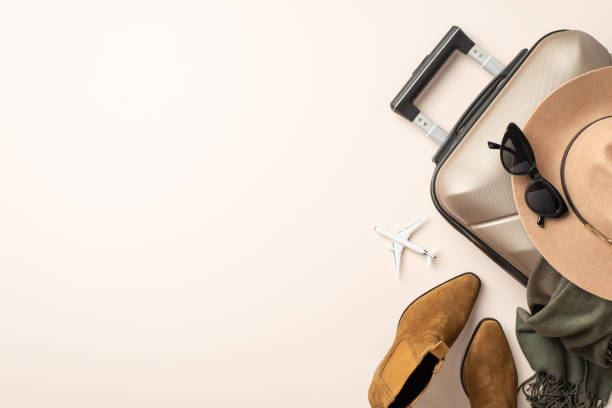 istock Sophisticated flying concept. Miniature plane model surrounded by classy items - felt hat, cat-eye shades, scarf, ankle boots, suitcase on neutral pastel background with empty space for advert 1669374317