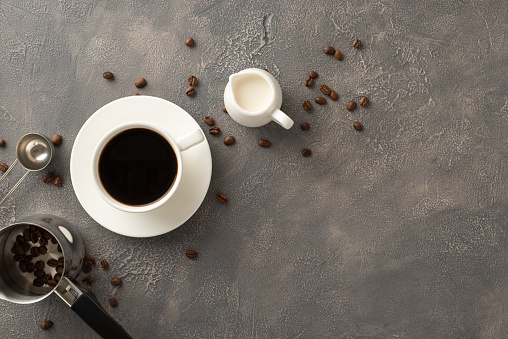 CafÃ© Creation: Top-down view of coffee beans, espresso cup, cream jar, coffee turk, measuring spoon on textured grunge backdrop with empty space for promo message