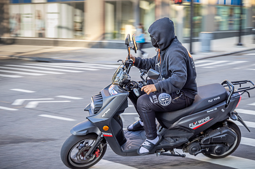 Queens Plaza, Long Island City, Queens, New York, USA - August 19th 2023:  Messenger man on a motorbike driving around a corner