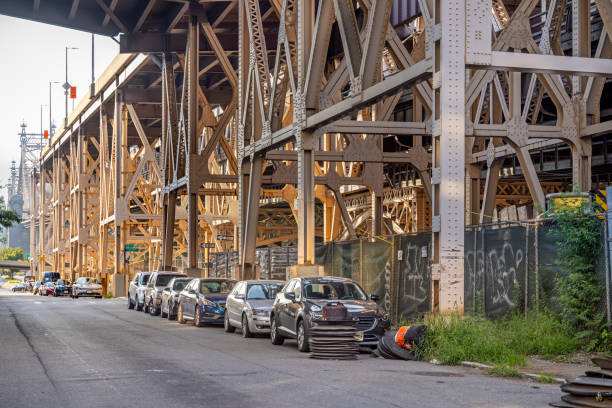 parked cars under a large steel bridge - queensborough bridge imagens e fotografias de stock