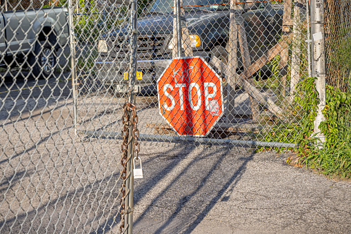 44th Drive, Long Island City, Queens, New York, USA - August 19th 2023: Stop sign and a mesh wire fence outside a parking lot on a sunny summers afternoon