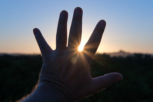 Backlit shot of man's open hand against horizon line at sunrise - dawn