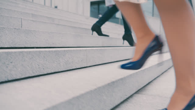 SLO MO An unrecognizable woman wears skirt and high heels in blue color while she walks up the stairs in front of a modern building