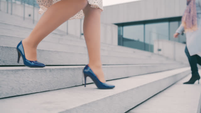 SLO MO An unrecognizable woman wears skirt and high heels in blue color while she walks down the stairs in front of a modern building