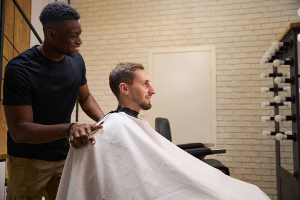 Young man sits in a barbers chair Young man sits in a barbers chair, an African American master chats with him in a friendly way black barber stock pictures, royalty-free photos & images