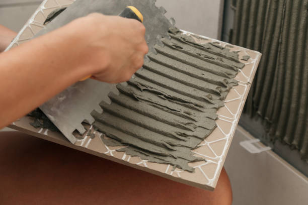 istock Woman tiling bathroom walls, applying adhesive on a tile and placing ceramic tile in right position. Process of installation of tiles in the bathroom step by step. DIY home improvement. 1669710330