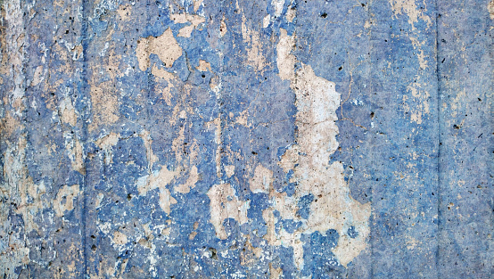 High Resolution old weathered bluish concrete wall detail, coated with multiple layers of white, beige and blue paints, applied through the years randomly one on top of the other, cracking and peeling off, run down by the elements, grunge background texture stock photo.