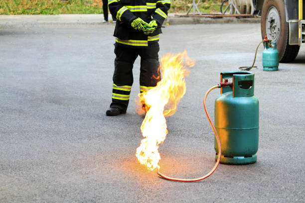 istock Fire burning on green gas container and Firefighter or fireman in black and green safety uniform or suit and extinguish fire on street with car wheel background and copy space. Conflagration and risk 1669766507