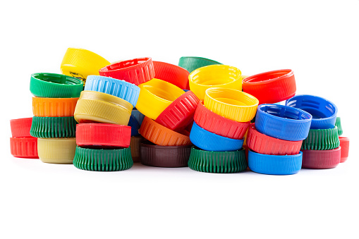 Different color bottle caps, excellent raw material for recycling. Composition with plastic bottles and caps isolated on white.