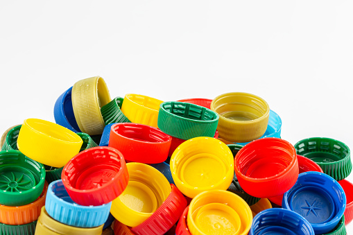 Different color bottle caps, excellent raw material for recycling. Composition with plastic bottles and caps isolated on white.