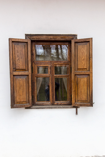 Window with wooden shutter in an old vintage house. Open front brown shutter window on white wall. Architecture.