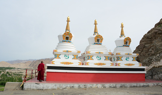 Ladakh, India - Jul 17, 2015. A monk praying near white stupas at the Tibetan monastery in Ladakh, northern India. Ladakh is one of the most sparsely populated regions in Jammu and Kashmir.