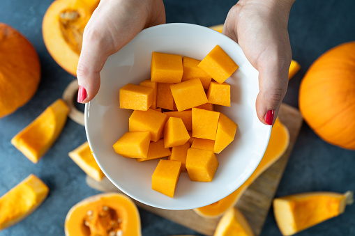 Woman holding diced butternut squash pumpkin. Female hands with sliced cubes, fresh raw pumpkins pieces. Preparing food, dicing ingredients for a seasonal autumn fall dish, soup or pie.