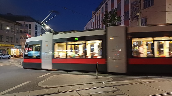 Frankfurt, Germany - October 28, 2020: Long exposure shot of an illuminated tramway at tram stop Willy-Brandt Platz in front of the Frankfurt theatre (Schauspielhaus) in the city center of Frankfurt at night. Some passersby in the background