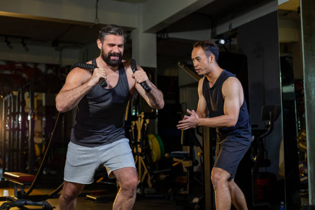 istock Caucasian man with strong and muscular body training on core weight training by rope pulling with his supporting trainer encouraging inside gym for advance exercise and workout concept 1669866317