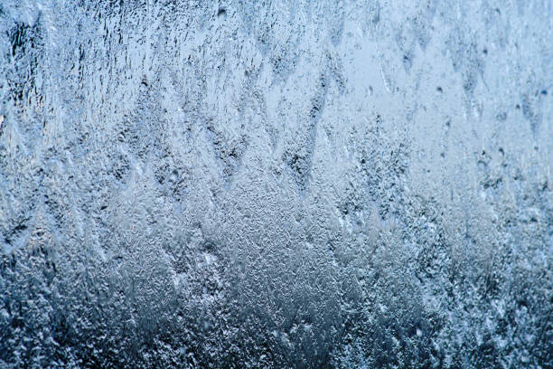 Intricate frost patterns covering a window pane against blue sky and bright sunlight