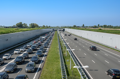 DELFT, NETHERLANDS - MAY 13, 2023 : Modern deepened motorway A4, traffic jam direction Rotterdam. Highway leading through a nature reserve between Delft and Rotterdam, Netherlands