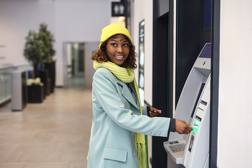 Young woman using an ATM in a shopping mall. About 25 years old, African female.