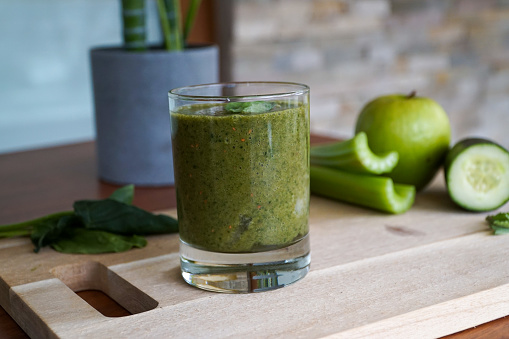 A refreshing green smoothie in a glass with fresh ingredients like spinach, banana, and cucumber beautifully displayed in the background.