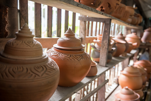 Orange Handicraft clay pot on wooden shelf in natural light by window in Ko Kret, Nonthaburi, Thailand.