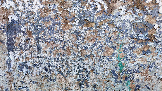 High Resolution old weathered bluish concrete wall detail, coated with multiple layers of various paints, applied through the years randomly one on top of the other, cracking and peeling off, run down by the elements, grunge background texture stock photo.