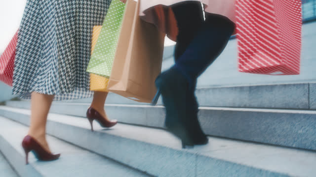 SLO MO Two unrecognizable women in stilettos carry shopping bags as they walk up the stairs in the city