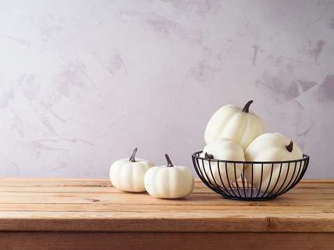 Wooden table with white pumpkin decoration in metal basket. Halloween or Thanksgiving holiday concept