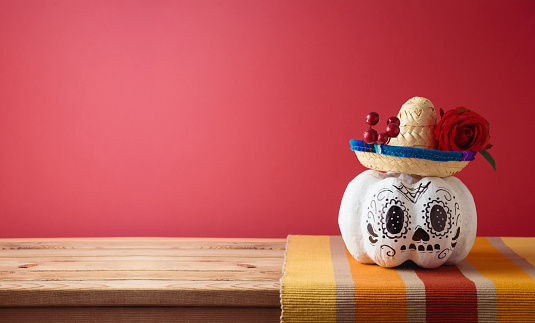 Day of the dead, Dia De Los Muertos holiday concept. Sugar skull Halloween pumpkin and Mexican party hat on wooden table over pink background