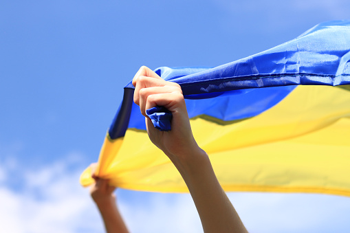A girl with a yellow-blue flag in her hands. The flag flutters in the wind. Patriotism. Yellow and blue flag of Ukraine in the woman's hands