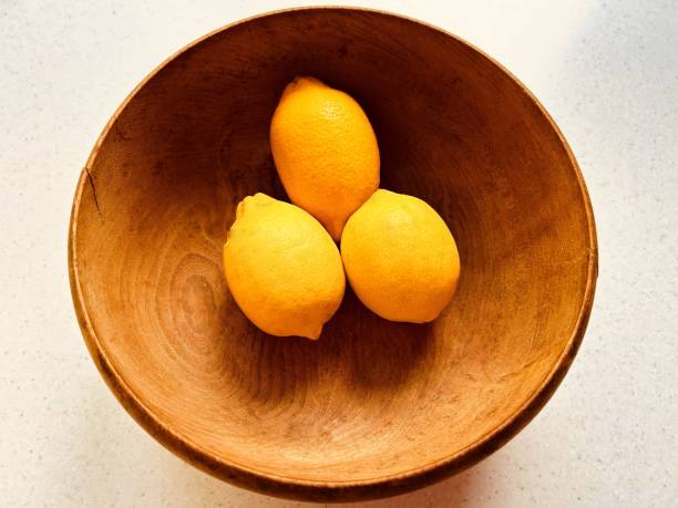 Three yellow lemons in a grained wooden bowl. Acidic, bitter, sour, nutritious fruit.