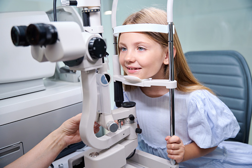 Smiling little patient holding her head against chinrest and forehead support during slit lamp exam