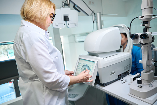 Vision specialist looking at adult patient eye image on autorefractor touch screen